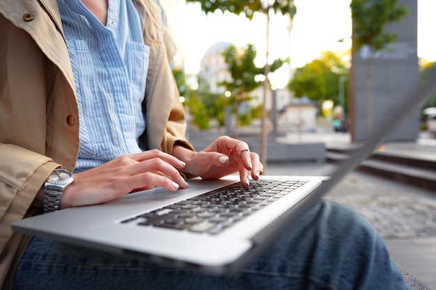 Close up of female hands typing on computer keyboard of a laptop sitting in the street