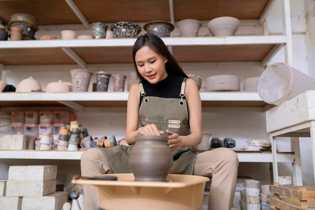 Close up of female hands working on potters wheelasian female sculpture woman shaping mold small vase bowl clay on potter's wheel at home studio workshop art and creation hobby concept