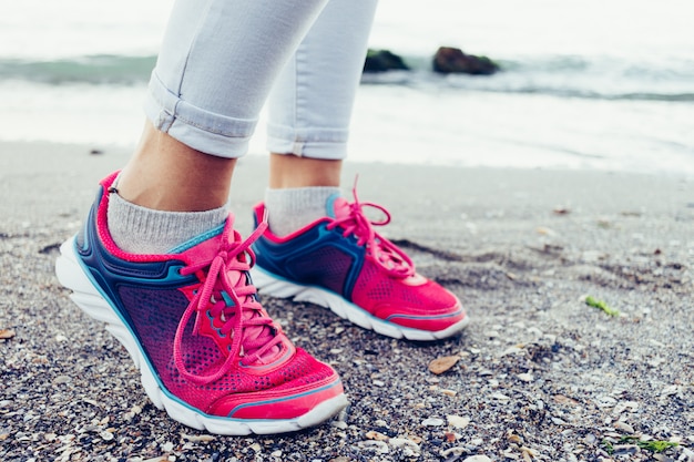 Close-up of female legs in sneakers and jeans on the beach near the water