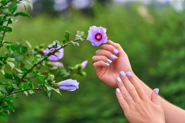 Close up on female manicure next to a hibiscus plant