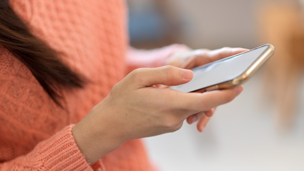 Close-up female in pink sweater holding, using modern smart mobile phone, blurred background.