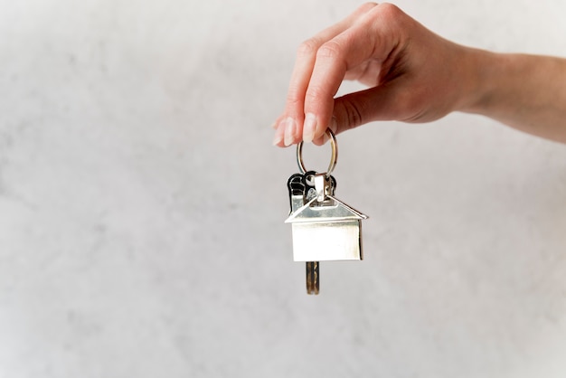 Close-up of female's hand holding silver house keychain against concrete wall