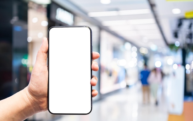 Close-up of female use Hand holding smartphone with empty blank white screen blurred images touch of Abstract blur of inside shopping complex background,shopping online concept.