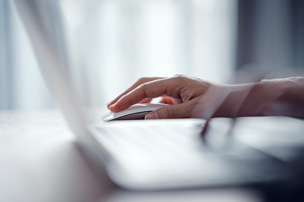 Close up finger of woman using modern white wireless mouse while working on laptop computer.