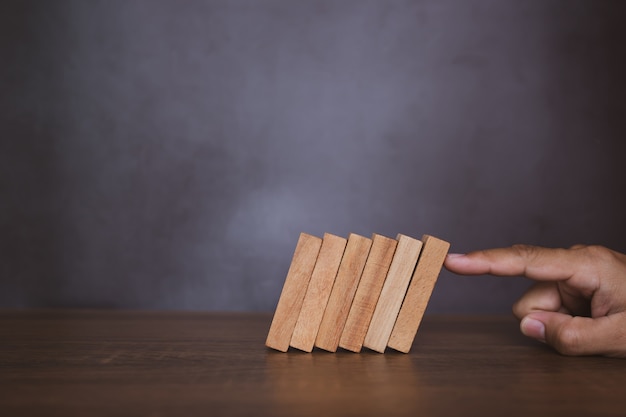 Close-up fingers prevent the wooden block from falling domino.