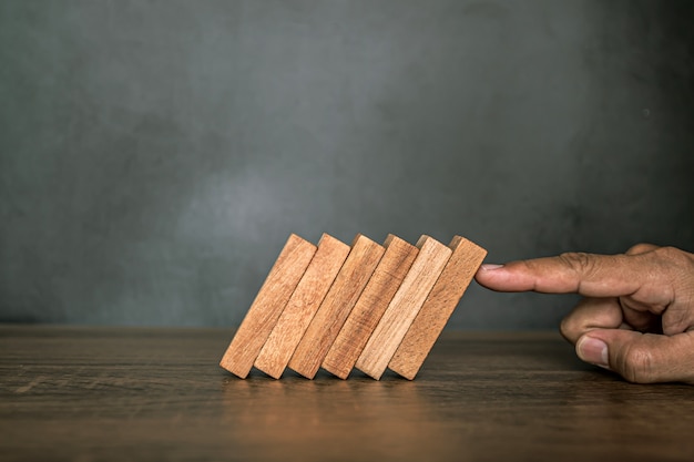 Close-up fingers prevent the wooden block from falling domino.