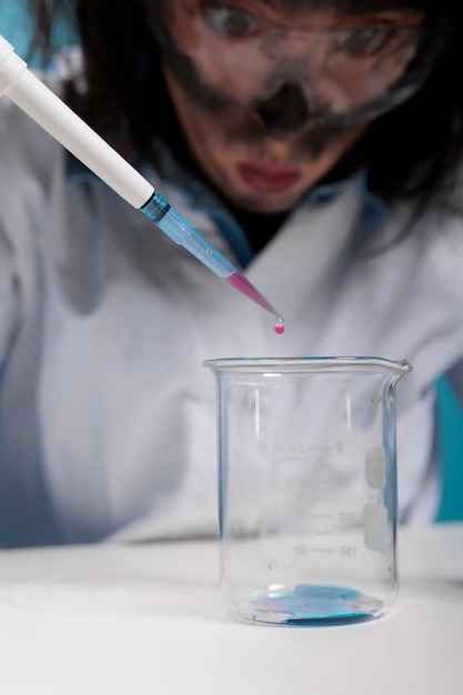 Close up of foolish mad looking scientist with pipette doing experiments while sitting at desk. Wacky insane chemist using dropper to mix experimental chemical compounds after lab explosion.