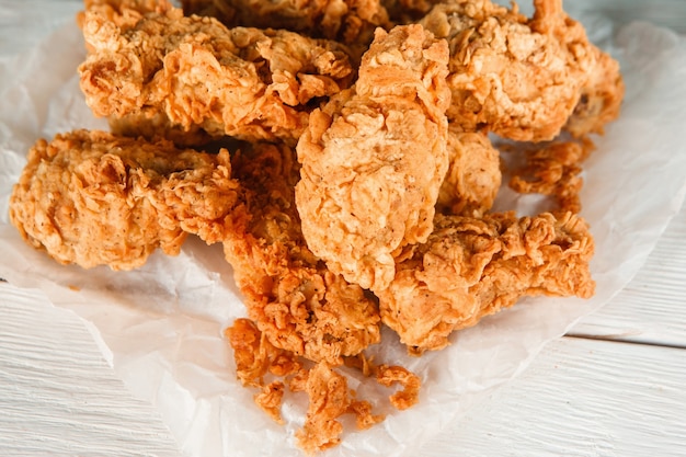 Close up fresh appetizing fried chicken on white paper on white wooden table background. Fast food, tasty meat snacks for beer.