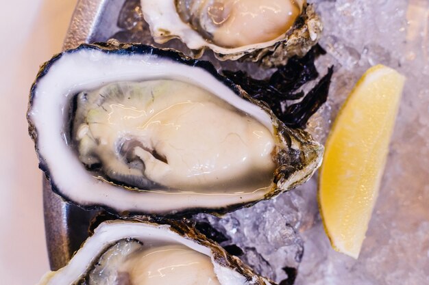 Close up fresh oysters served on ice in steel plate with sliced of lemon and spicy sauces.