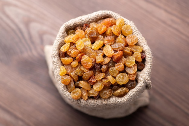 Close up of fresh tasty raisin in small cloth bag on wooden background