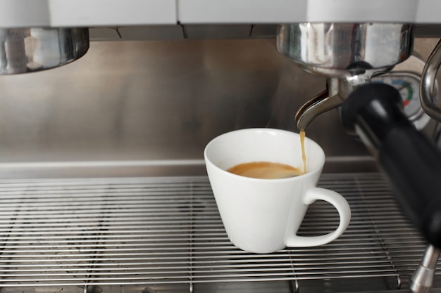 Close-up of freshly brewed coffee is poured from a coffee machine into a white cup