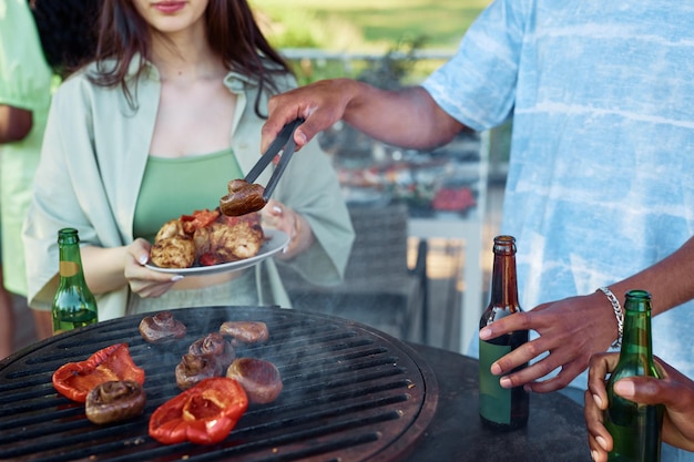 Close up of friends grilling vegetables while enjoying vegetarian barbeque party outdoors in summer