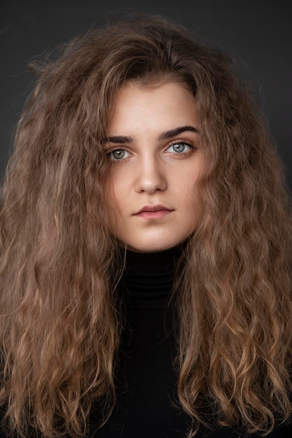 Close up front portrait of a young woman with curly hair wear black suitcase isolated dark background