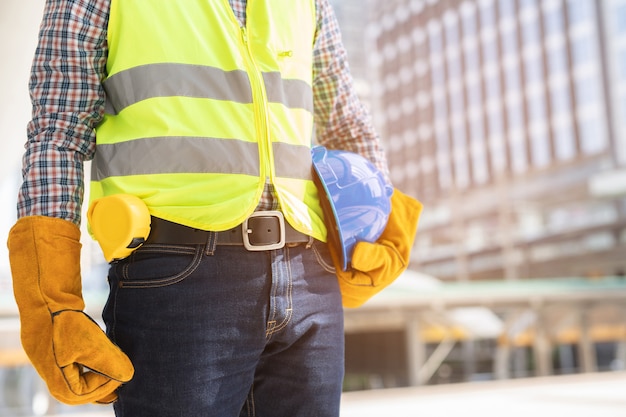 Close up front view  engineering male construction worker stand holding safety blue helmet and wear gloves with reflective clothing