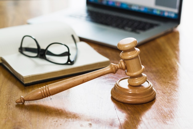 Photo close-up of gavel; book; laptop and spectacles on wooden desk