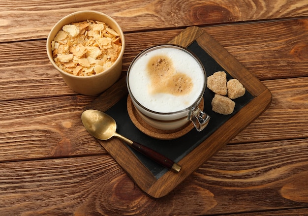 Close up glass cup of cappuccino coffee with heart shaped latte art and Napoleon mille-feuille vanilla custard slice cake, on black slate over wooden table, high angle view