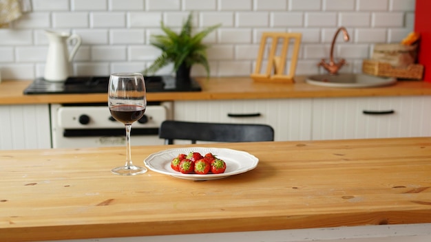 Close up of glass of wine with strawberries on plate on table in kitchen Concept of dating