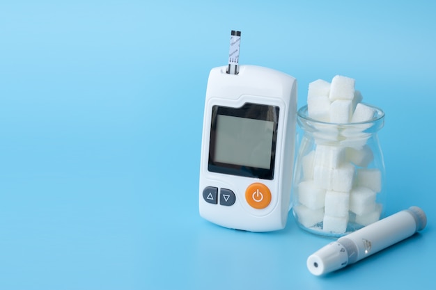 Close up of Glucose meter, lancet and jar of sugar cubes on blue backgrounds.