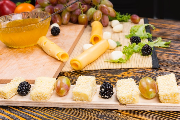 Photo close up of gourmet cheeses and fresh fruits arranged on narrow board with cutting board and ingredients in background