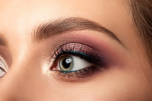 Close up of green woman eye with beautiful brown with red and orange shades smokey eyes makeup modern fashion make up studio shot