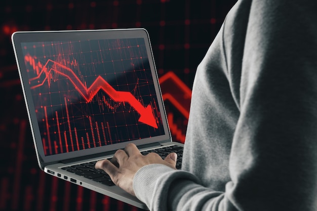 Close up of hacker hands using laptop with red candlestick arrow going down on blurry background Economic recession and crisis concept Double exposure