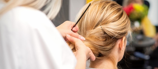 Close-up hairdresser styling blonde hair on the back of the head in a beauty salon.