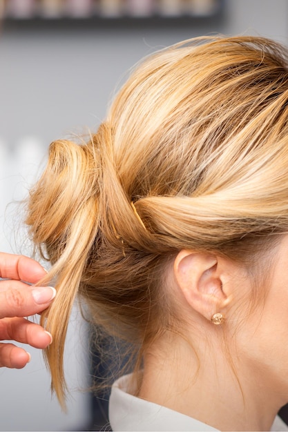 Close-up hairdresser styling blonde hair on the back of the head in a beauty salon.