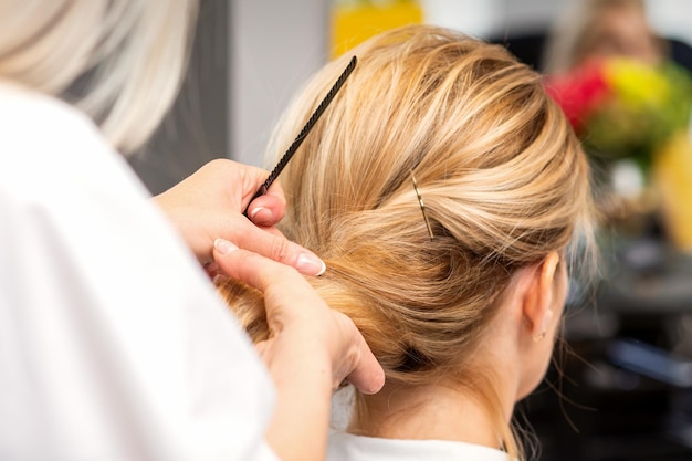 Close-up hairdresser styling blonde hair on the back of the head in a beauty salon.