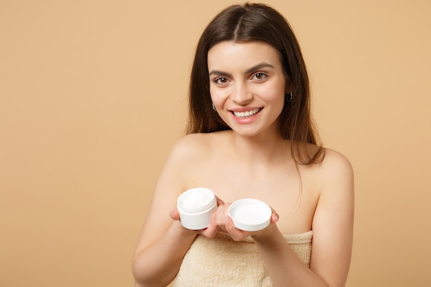 Close up half naked woman with perfect skin nude make up applying facial cream isolated on beige pastel wall