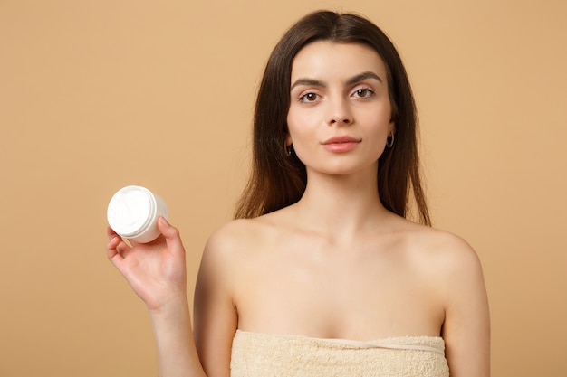 Close up half naked woman with perfect skin nude make up applying facial cream isolated on beige pastel wall