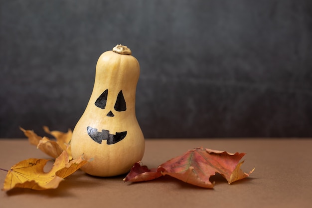 Photo close up of a halloween pumpkin with painted black eyes and mouth and dry maple leaves