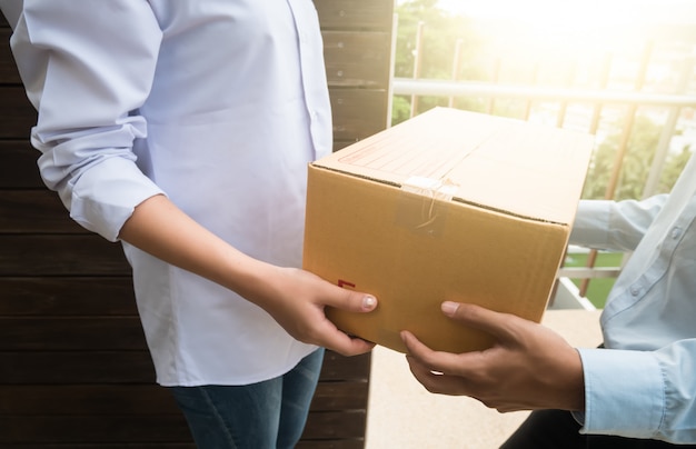 Close up hand of asia woman are receive a box from delivery man with sun light