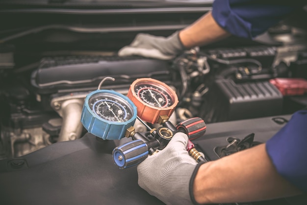 Close up hand of auto mechanic using measuring manifold gauge check the refrigerant and filling car air conditioner for fix and checking for repair service support maintenance and car insurance