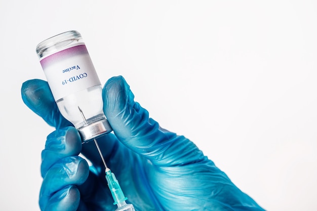 Close-up of a hand in blue medical gloves holding a medical syringe and vial with COVID-19 vaccine