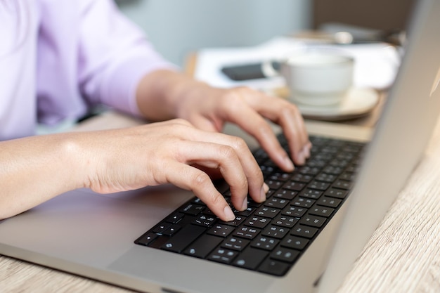 Close up hand of a business woman typing keyboard laptop computer on desk office