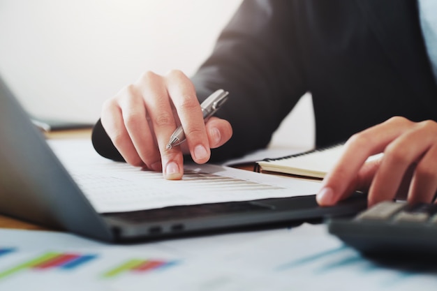 Close-up hand of businessman analyzing investment chart on paperwork with laptop in office. 