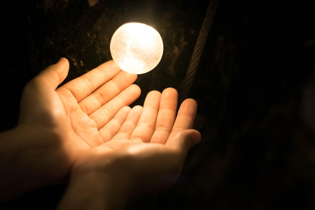 Close-up of hand by illuminated light bulb against black background