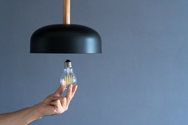 Close-up. A hand changes a light bulb in a stylish loft lamp. Spiral filament lamp. Modern interior decor.