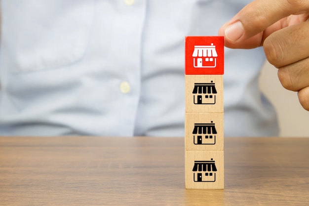 Close-up hand choose cube wooden toy blocks stacked with franchise business store icon.