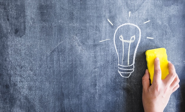 Close-up of hand cleaning the light bulb drawn on blackboard with duster