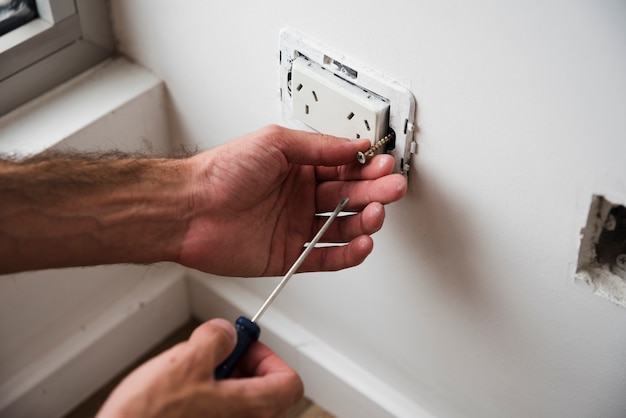 Close-up of hand fixing plug socket using screwdriver