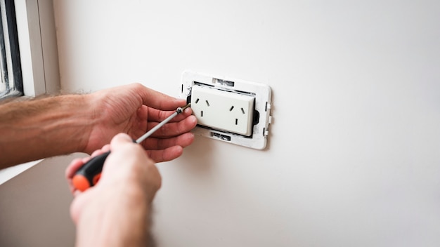 Close-up of hand fixing plug socket on white wall