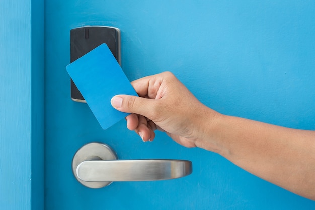 Close up hand holding blue hotel keycard in front of electric door