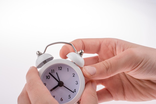 Close-up of hand holding clock against white background