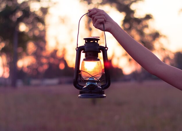 Photo close-up of hand holding illuminated lantern during sunset