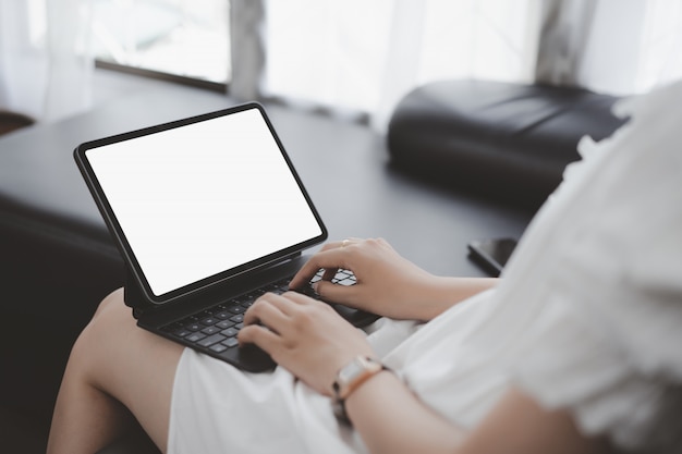 Close-up of hand holding mockup white screen tablet on sofa in living room.