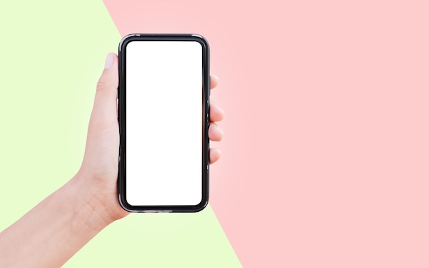 Close-up of hand holding smartphone with white mockup isolated on two surfaces of green and red colors.