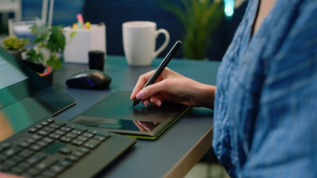 Close up of hand holding stylus on graphic tablet for pictures retouch at desk. Photographer using editing equipment on photos for retouching project in photography studio. Editor with gadget