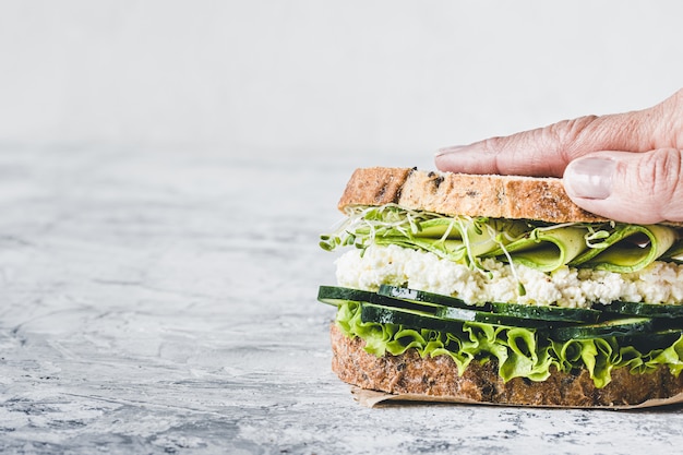 Photo close-up of a hand holding a vegetarian sandwich with green vegetables. lettuce, zucchini, alfalfa and cucumber. vegan food