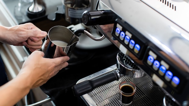 Close up hand holding Whipped cream with coffee. Making a cup of coffee in a coffee machine, the steam and the cup. Espresso maker machine with portafilter close up. Concept Coffee maker in cafe.